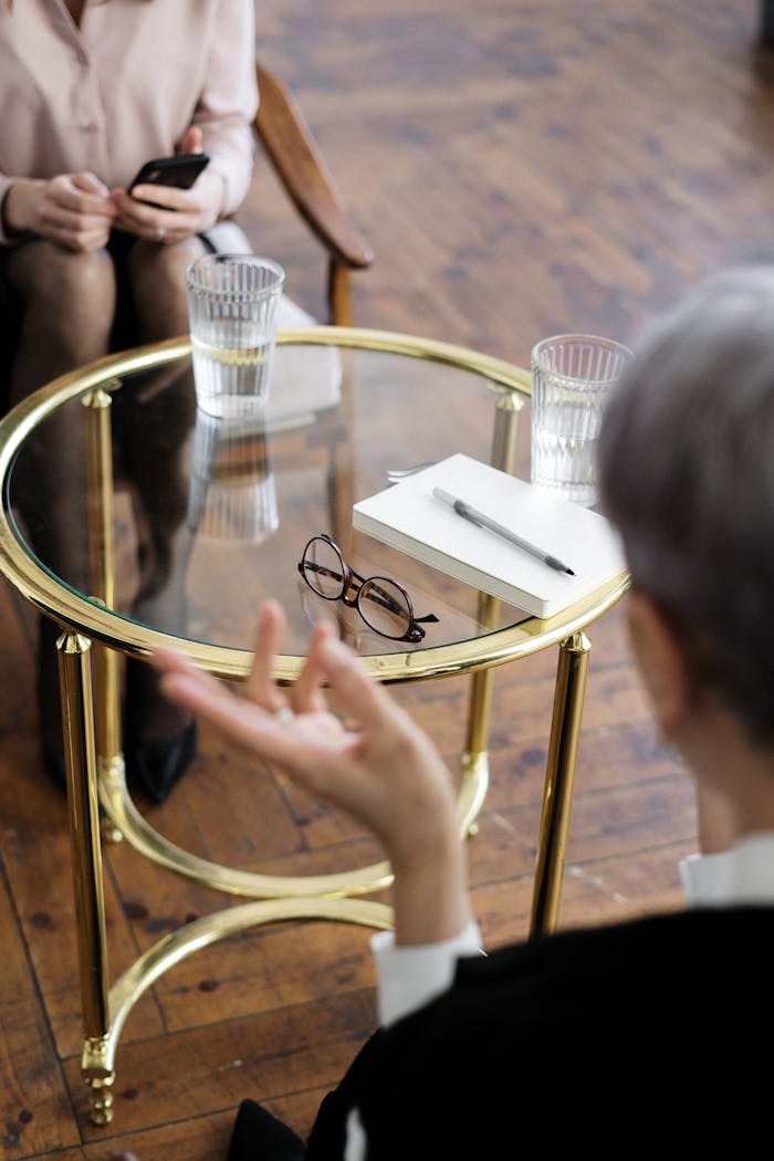 Home Two adults engaged in a therapy session, seated at a glass table with notebooks and water glasses.
